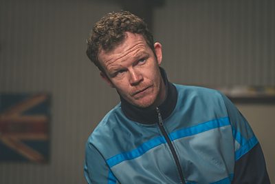 A man in a tracksuit with a union flag behind him