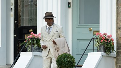  Lennie James as Barrington Walker dressed in a suit, walking down steps and away from a front door.