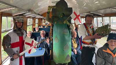 A man dressed as an asparagus, with a man dressed as St George shown on board a steam train