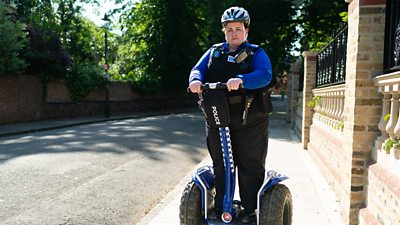 Jessica Gunning in character as Diane Pemberley, dressed in police uniform and stood on a police-branded Segway. 