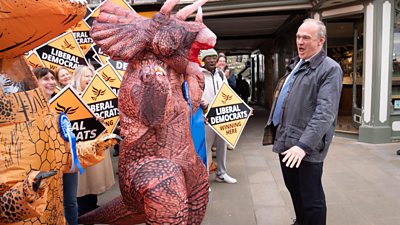 Liberal Democrats leader Sir Ed Davey wit playas up in dinosaur costumes