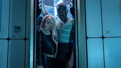 The Doctor and Ruby Sunday poke their heads out of a lift door, looking curious