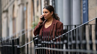 Lucie Shorthouse (Siobhan Clarke) holds a mobile to her ear and stands on the steps to a terraced house. 