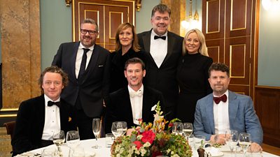 Tom Kitchin, Daniel Clifford, Tracey MacLeod, Adam Handling, Nathan Outlaw, Anna Haugh, Robin Gill smile to camera from a table at the MasterChef 20th Anniversary Dinner.