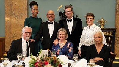 Franc Roddam, April Jackson, Gregg Wallace, India Fisher, William Sitwell, Nieves Barragan Mohacho, Monica Galetti smile to camera from a table at the MasterChef 20th Anniversary Dinner.