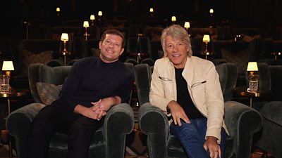 Jon Bon Jovi sits next to Dermot O’Leary in a cinema screening room. 