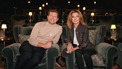 Shania Twain sits next to Dermot O’Leary in a cinema screening room. 