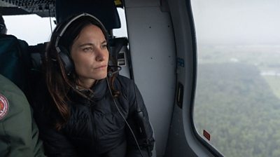 A woman, Ione Wells, looks out of the window in a helicopter