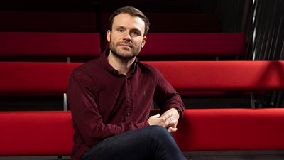 Jon Petrie sits on a red curved bench