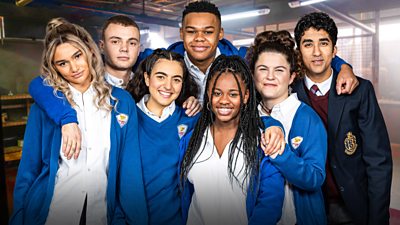 The cast of Phoenix Rise in their school uniform smiling to the camera