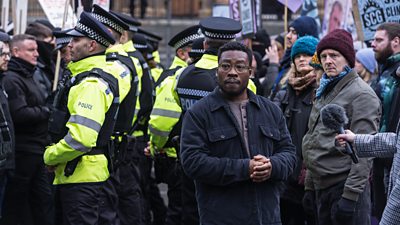 Fisayo Akinade stands in front of a crowd of police officers and protestors. 