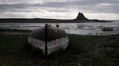 An overturned boat on the shore of Holy Island, with the castle visible in the background