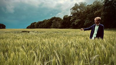 Charlie Cooper stands in a large field with his arm outstretched. 