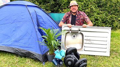 Andy Bennett in front of a tent with a kitchen sink, pot plant, mug tree and weights