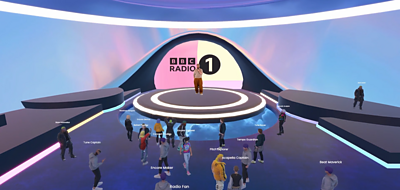 A performer stands on a virtual stage in a ý Radio 1 themed virtual room, surrounded by avatars of people in an audience watching the performance