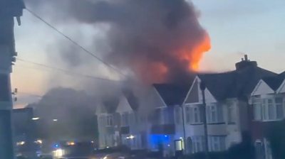 Flames and smoke from the roof of a residential house with flashing blue lights in the street