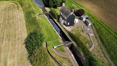 A canal lock in the middle of the countryside next to a black house surrounded by fields