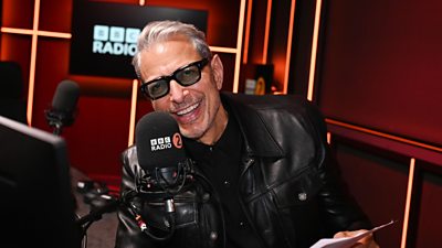 Image of Jeff Goldblum smiling in the studio with a radio 2 microphone in front of him 