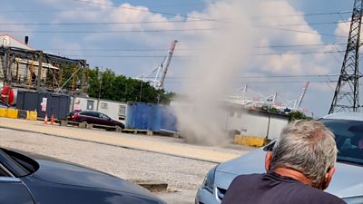 A dust devil - a column of dust spinning in the wind is watched by a man in a car park