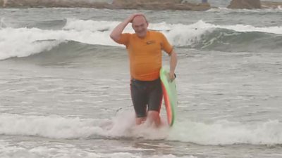 Sir Ed Davey holding a surfboard in the sea