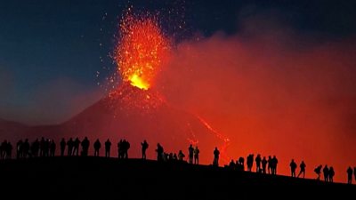 Hikers look on as Mount Etna erupts against the night sky