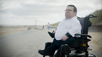 a man in a electronic wheelchair looking to the distance. beach in the background