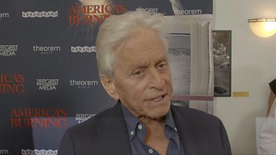 Michael Douglas wearing an open collar shirt, his hair is gray