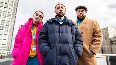 Lucia Keskin, Hugo Chegwin and Big Zuu looking to camera. They're outside with high rise flats in the background all wearing coats