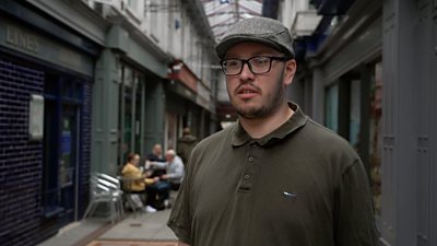 Man with flat cap and polo shirt standing in arcade