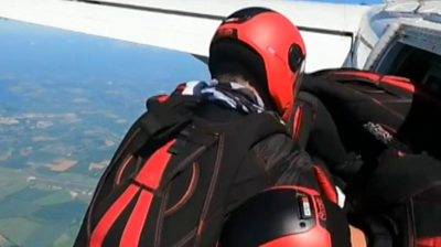 Two skydivers prepare to jump out of a plane on a sunny day, over countryside