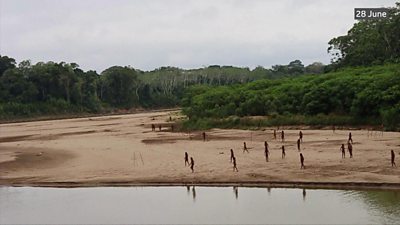 Wide shot of the bank of the Las Piedras River with dozens of the Mascho Piro tribe walking