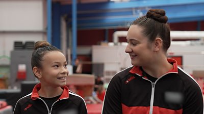 Two young gymnasts smile at each other at their club.