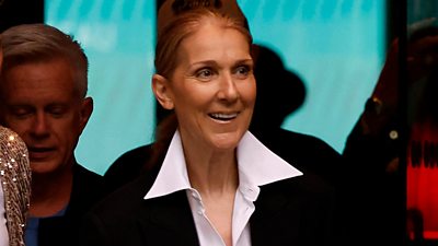 Celine Dion smiles as she walks out of the hotel
