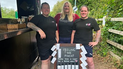 Three women stood around a black board with tickets on it.