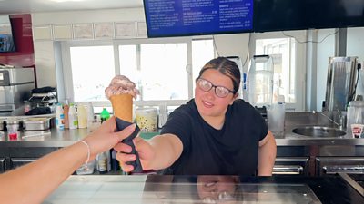 woman in an ice cream shop handing a cone to a customer