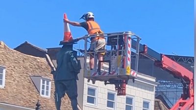 Man standing on a cherry picker removes cone from the top of a statue of Oliver Cromwell in St Ives town centre