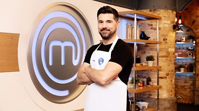 Craig Doyle in the MasterChef kitchen wearing an apron in front of the MasterChef logo