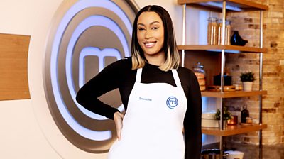 Snoochie Shy in the MasterChef kitchen wearing an apron in front of the MasterChef logo