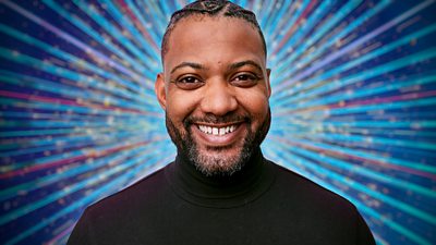 JB Gill wears a dark roll neck top and smiles for the camera