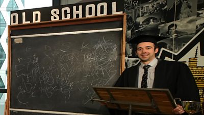 a man in an old fashioned teacher's gown and mortar board in front of a blackboard