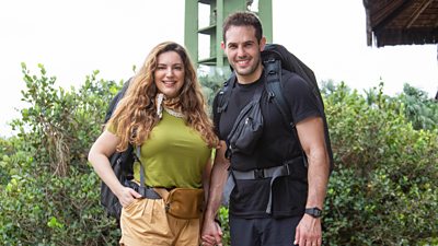 Kelly Brook and her husband Jeremy stand smiling for the camera wearing backpacks