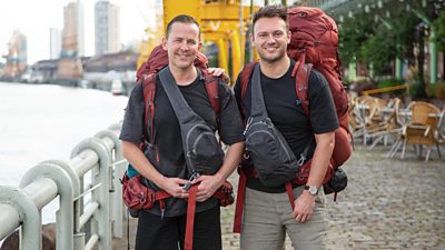 Scott Mills and his husband Sam stand by a boy of water wearing backpacks