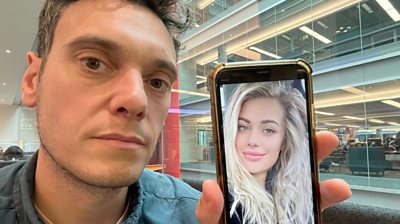 Joe Tidy holding a phone with the picture of a blonde woman