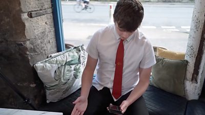 Student wearing a white shirt and red tie looks down at his mobile phone screen