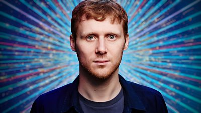 Jamie Borthwick wears a dark blue t-shirt and a dark blue shirt. He's pictured in close up with head and shoulders visible against a sparkling blue background.