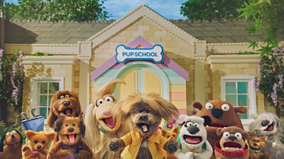 CBeebies House favourite Dodge with eleven other puppets in front of a building with ‘Pup School’ written above the door. 