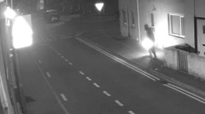 Black and white footage of CCTV shows a figure with an ignited petrol bomb seconds before it was thrown