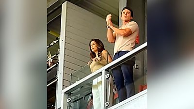 Eva Longoria and Rob McElhenney leaning over the barrier of the executive box