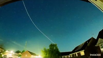 The white line of a meteor trail cuts across a blue night sky