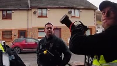 Three police officers on a street while one of them holds a battering ram above their head